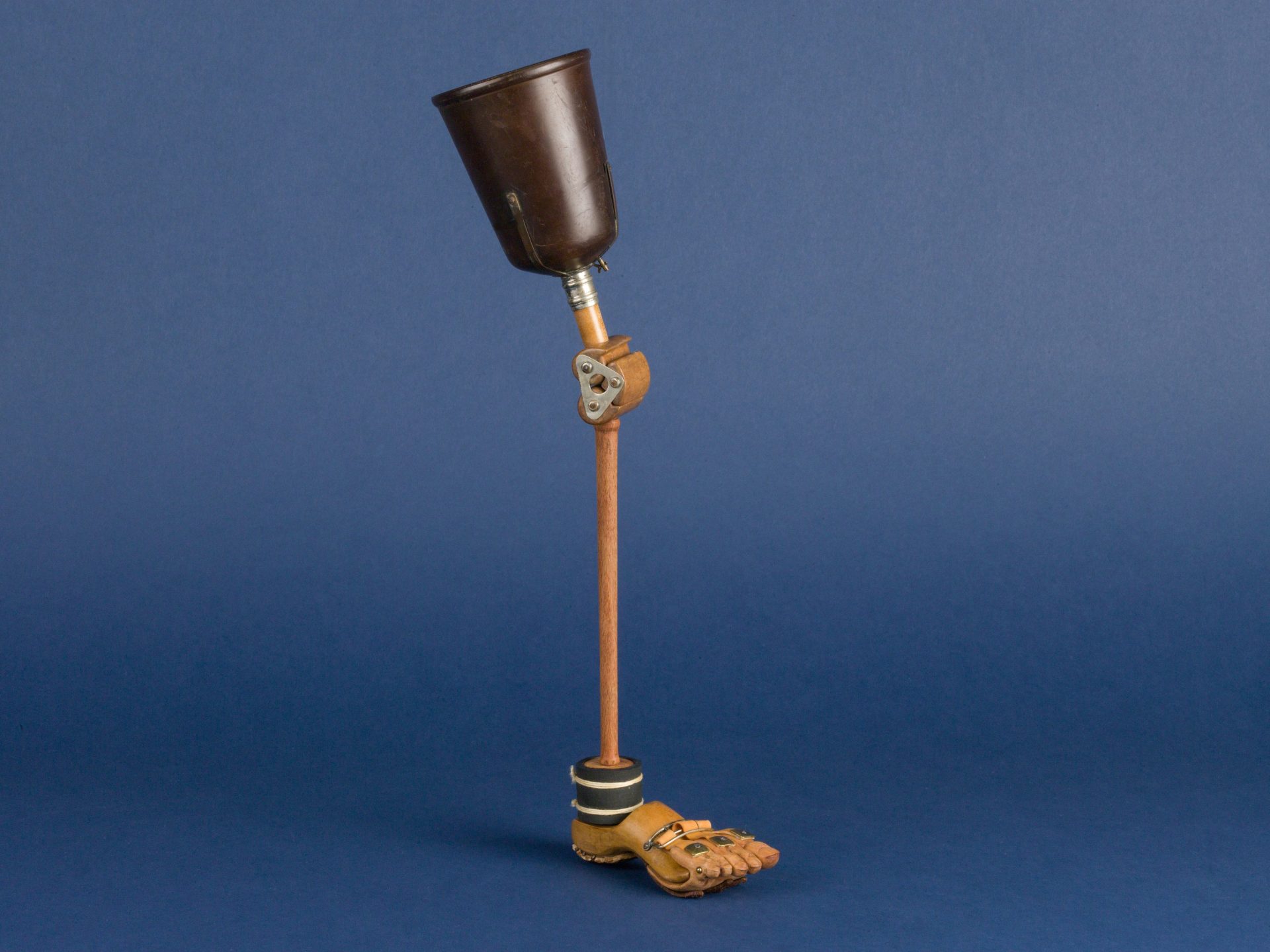 A prosthetic leg stands upright against a solid blue background.